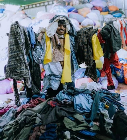 Textile recovery worker in yellow vest sorting through organized textile waste in processing facility